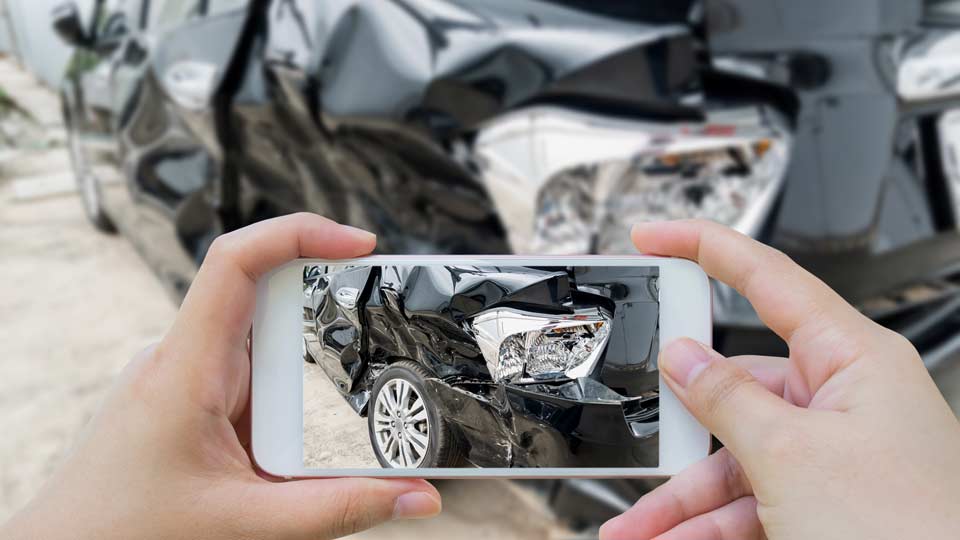 Unfallwagenankauf Pfaffenhofen: Unfallschaden an einem Auto wird mit dem Smartphone fotografiert.